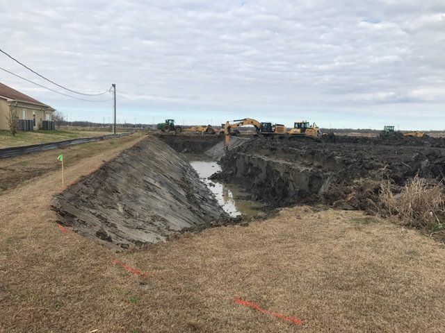 A group of construction vehicles are digging a large hole in a field.