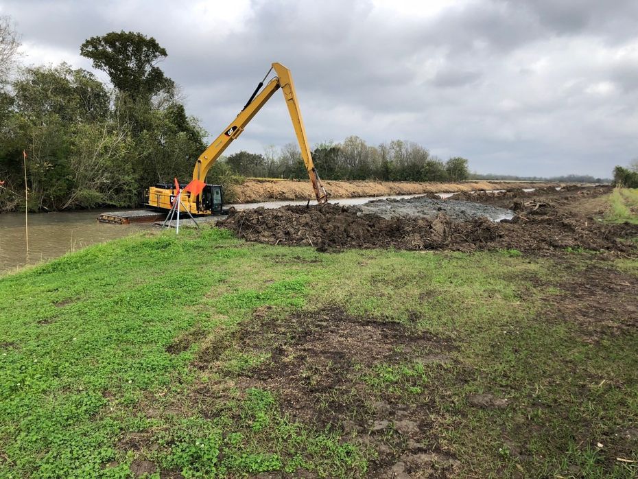 A large yellow excavator is digging a hole in a field.