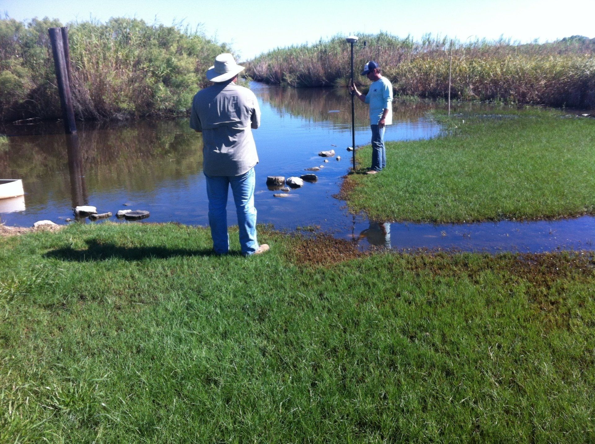 Two men are standing in the grass near a body of water