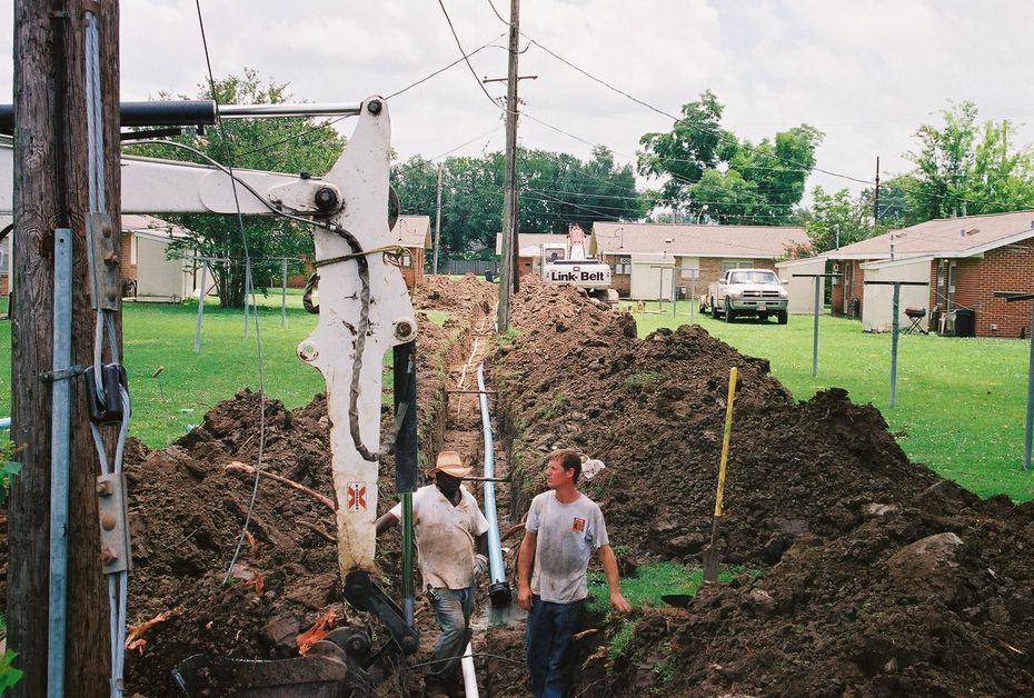 Two men are standing in a pile of dirt near a telephone pole