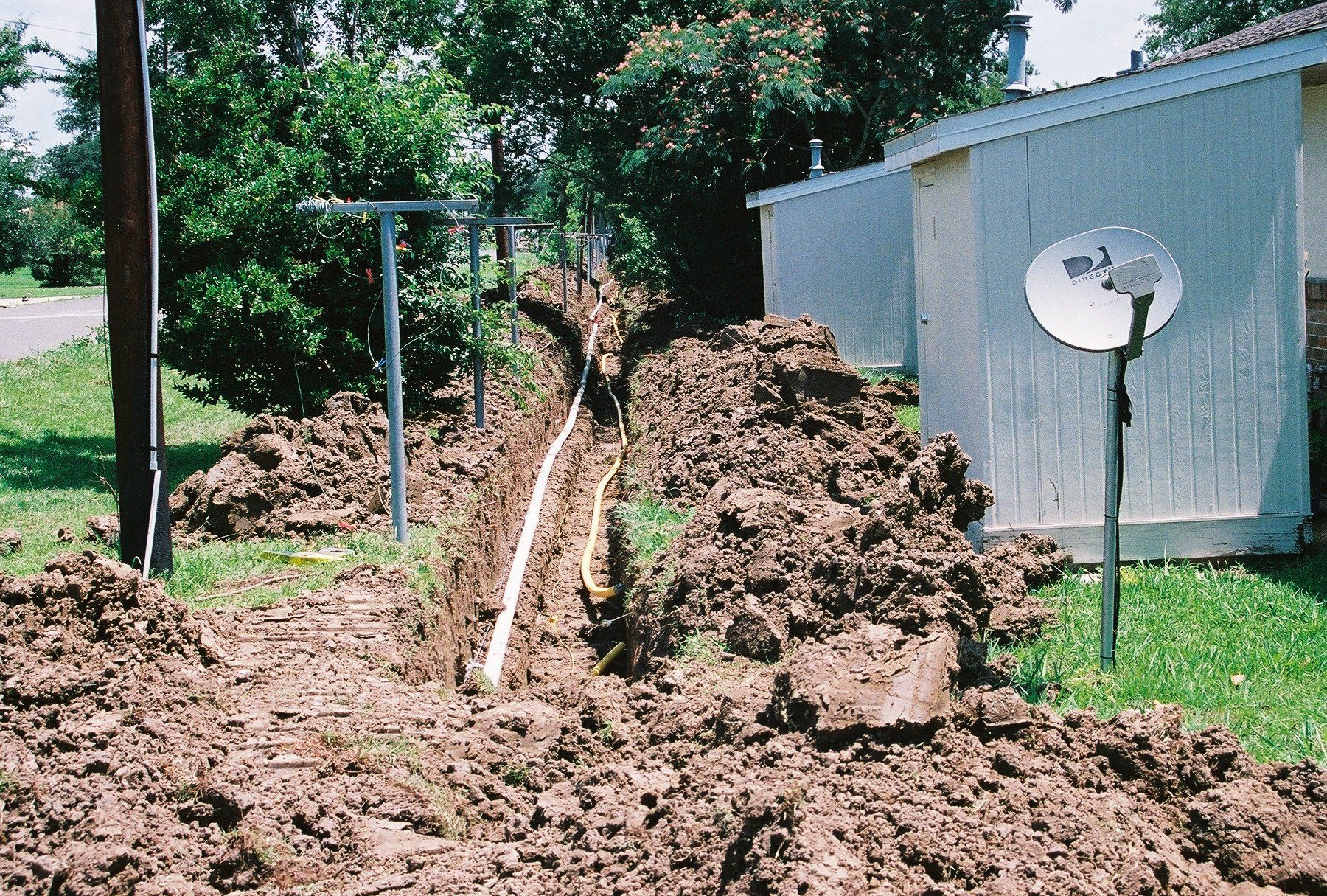 A satellite dish is sitting in the dirt in front of a house