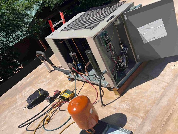 An air conditioner is being installed on a roof with a ladder in the background.