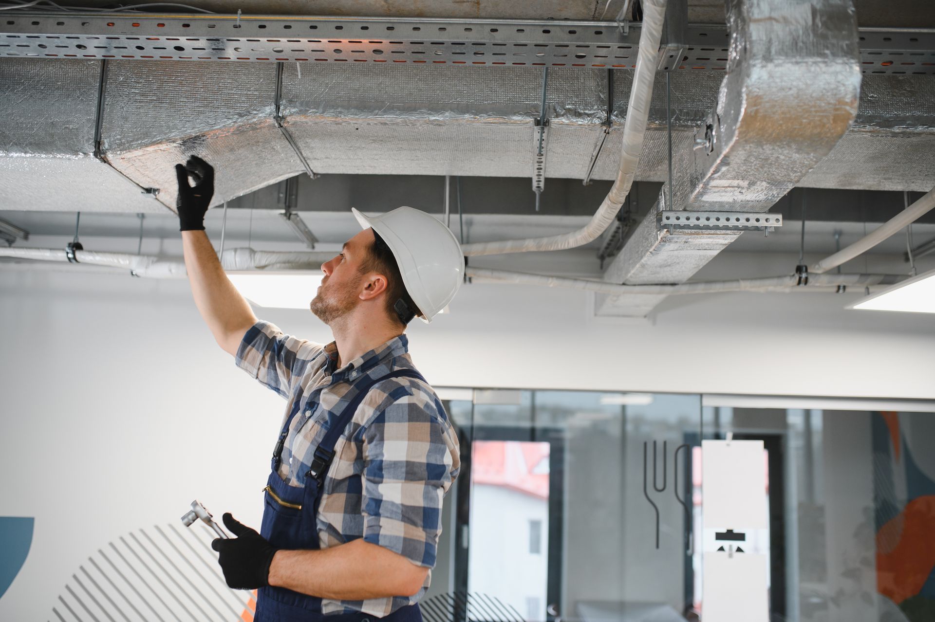 Worker inspecting ceiling ductwork in a bright office interior