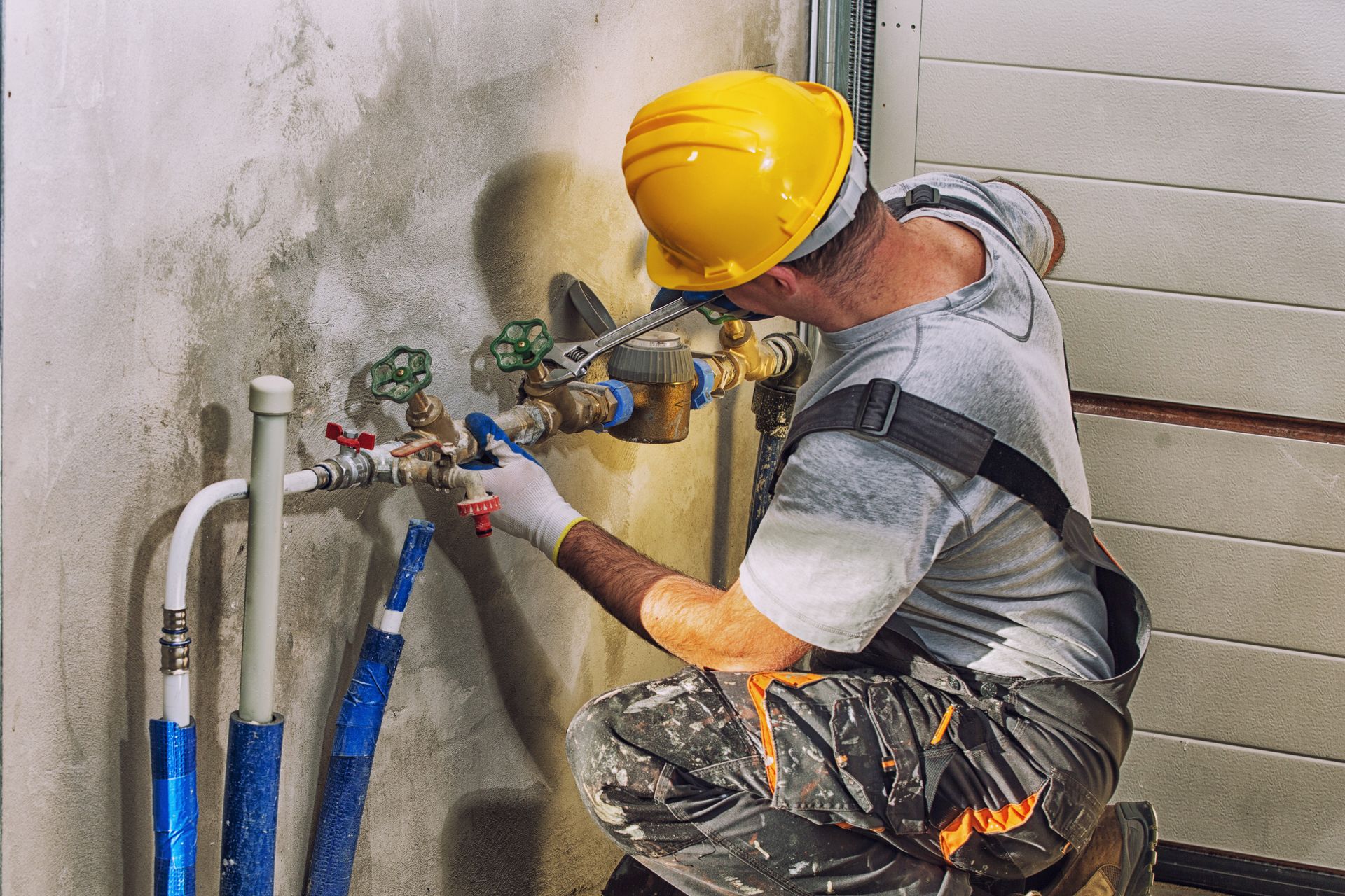 Worker in yellow hard hat installing plumbing pipes against a wall