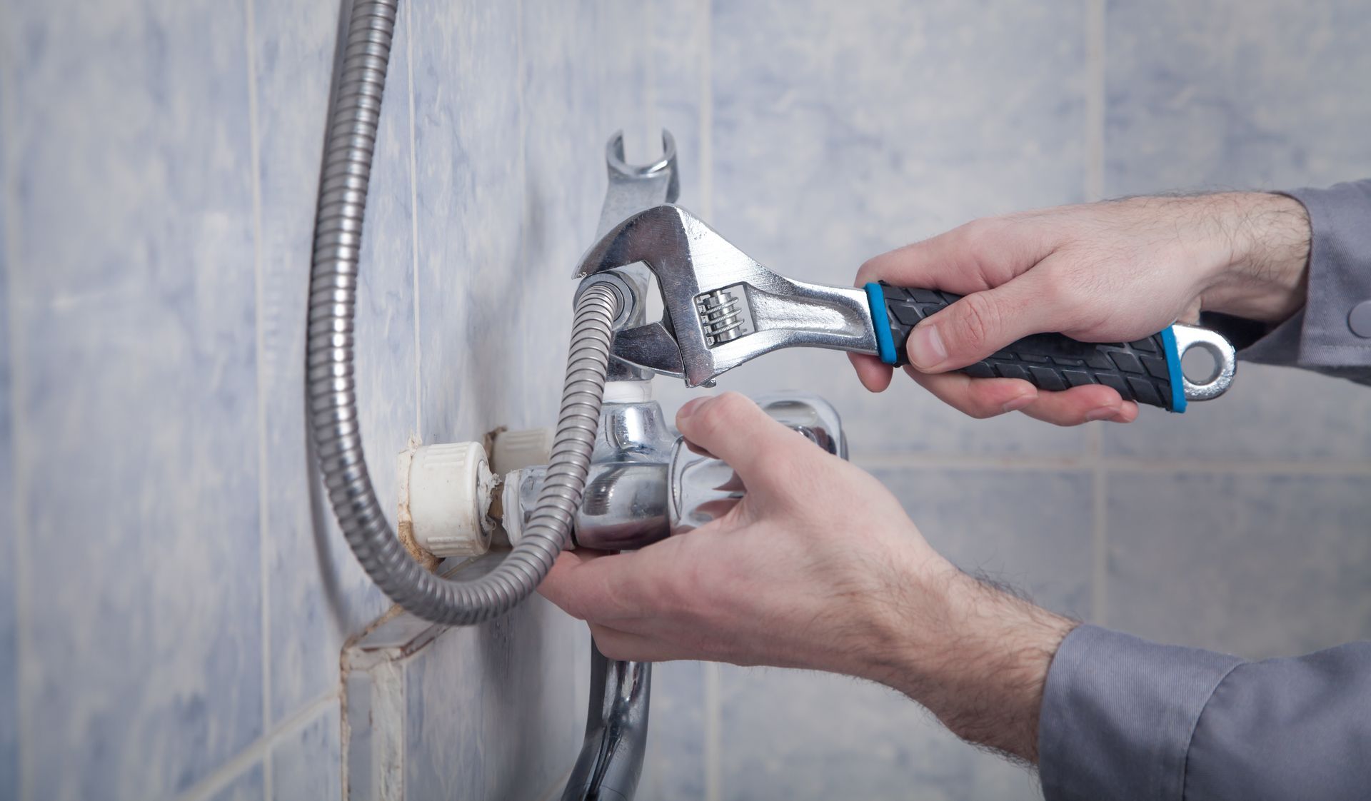 Hands adjusting a shower valve with a wrench and pliers on a tiled wall