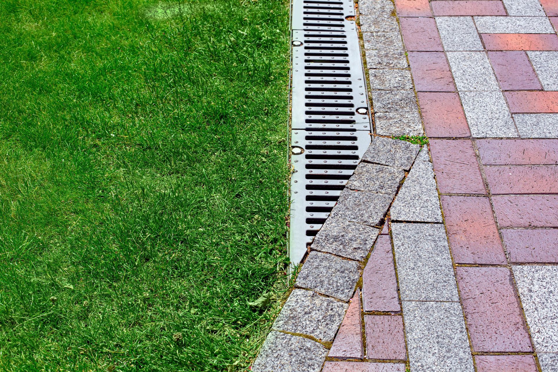 Grass beside a paved walkway with a drainage grate running along the edge