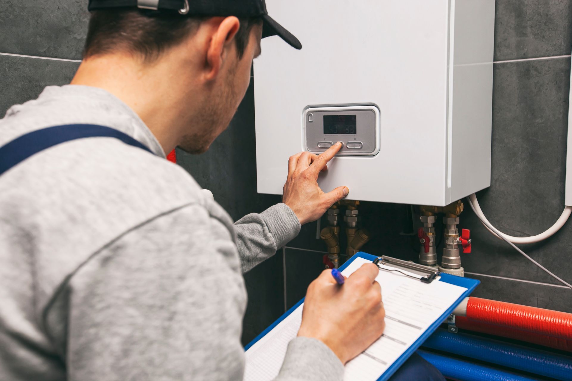Technician checking a wall-mounted boiler with a clipboard in a utility room