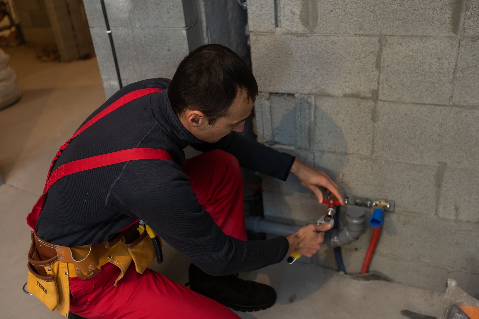 Plumber installing a wall pipe fitting near a concrete block wall using a wrench