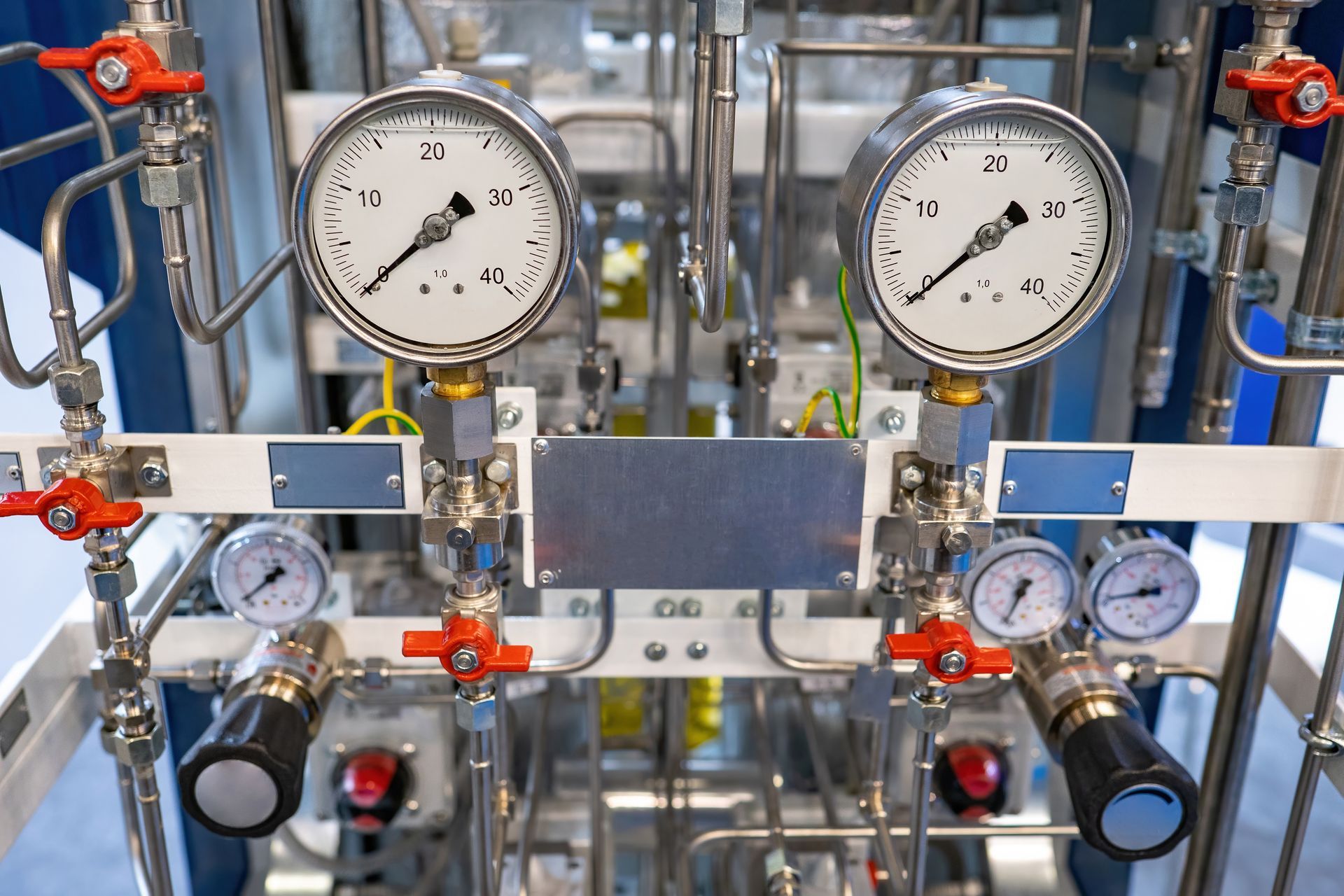 Industrial gauges and valves on a metal control panel with red handles and blue pipes