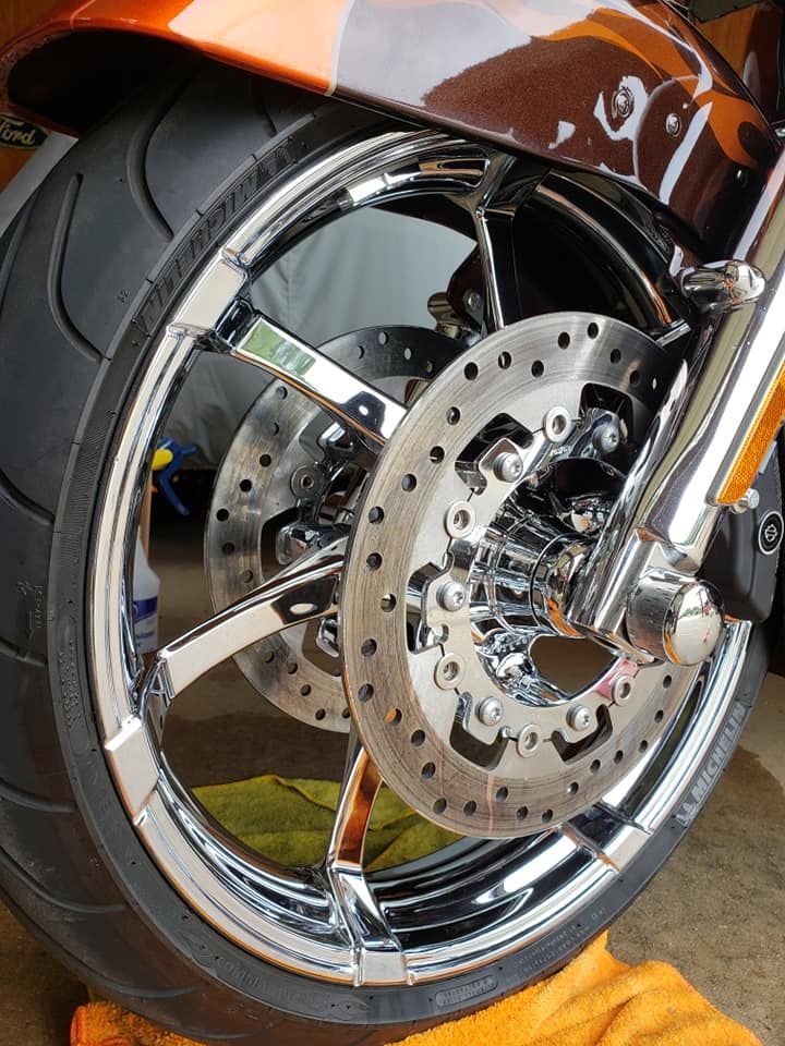 Shiny chrome motorcycle wheel with two disc brakes, tire, and orange accents.