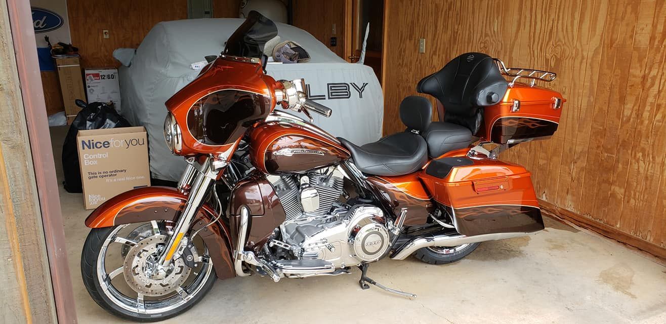 An orange and brown Harley-Davidson motorcycle parked inside a wooden garage, with a car cover in the background.