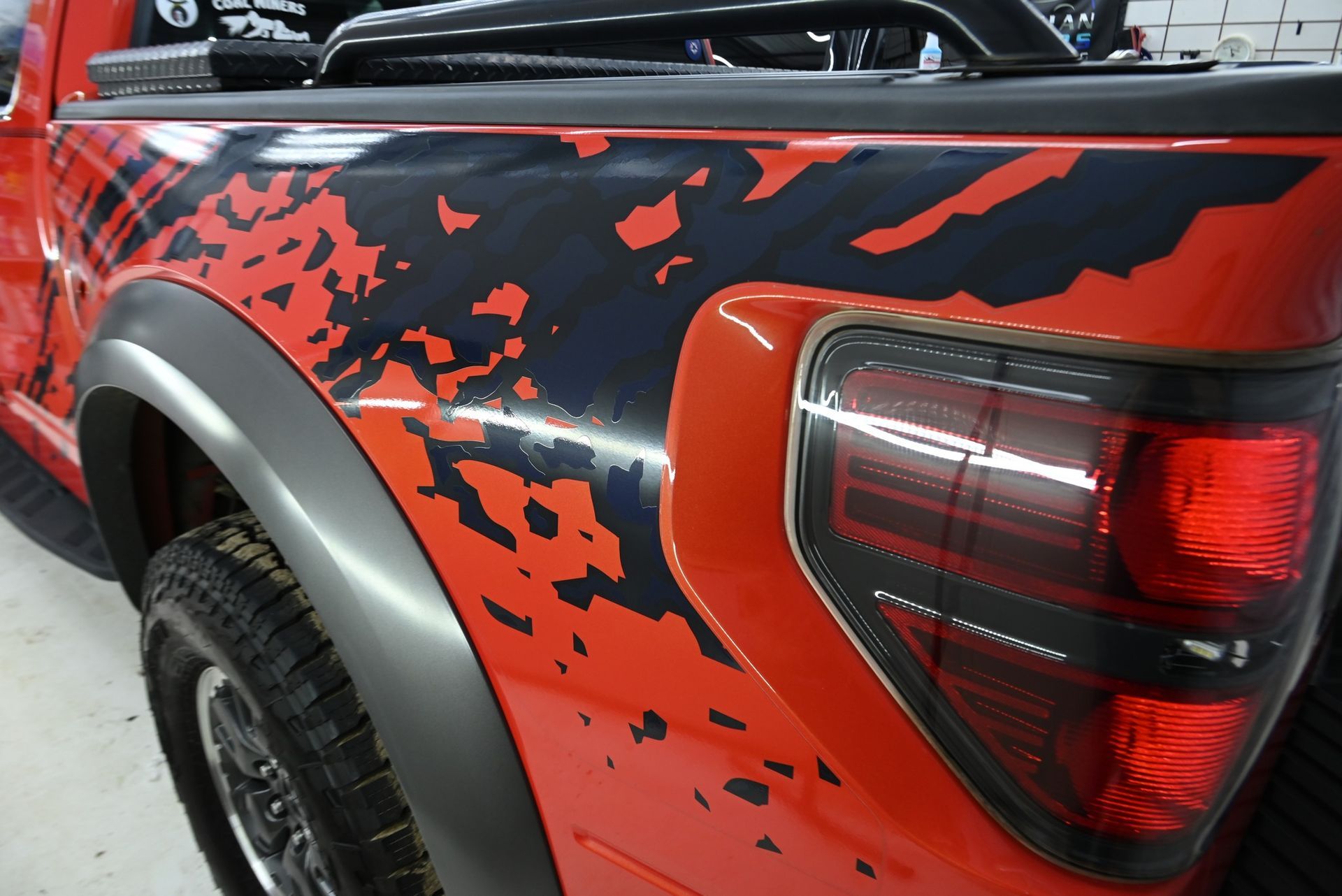 Red pickup truck with black graphics on the side, showing the rear tire and taillight.