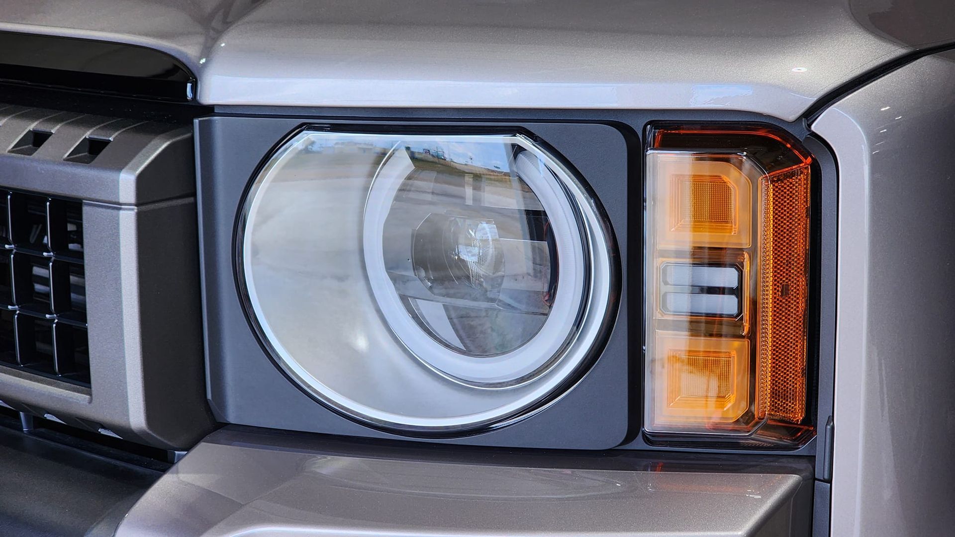 Close-up of a car headlight, featuring a round inner light with a white halo and an orange rectangular light.