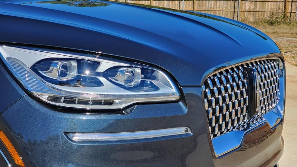 Blue Lincoln SUV's front. Headlight, chrome grille, and hood visible. Sunny outdoor setting.
