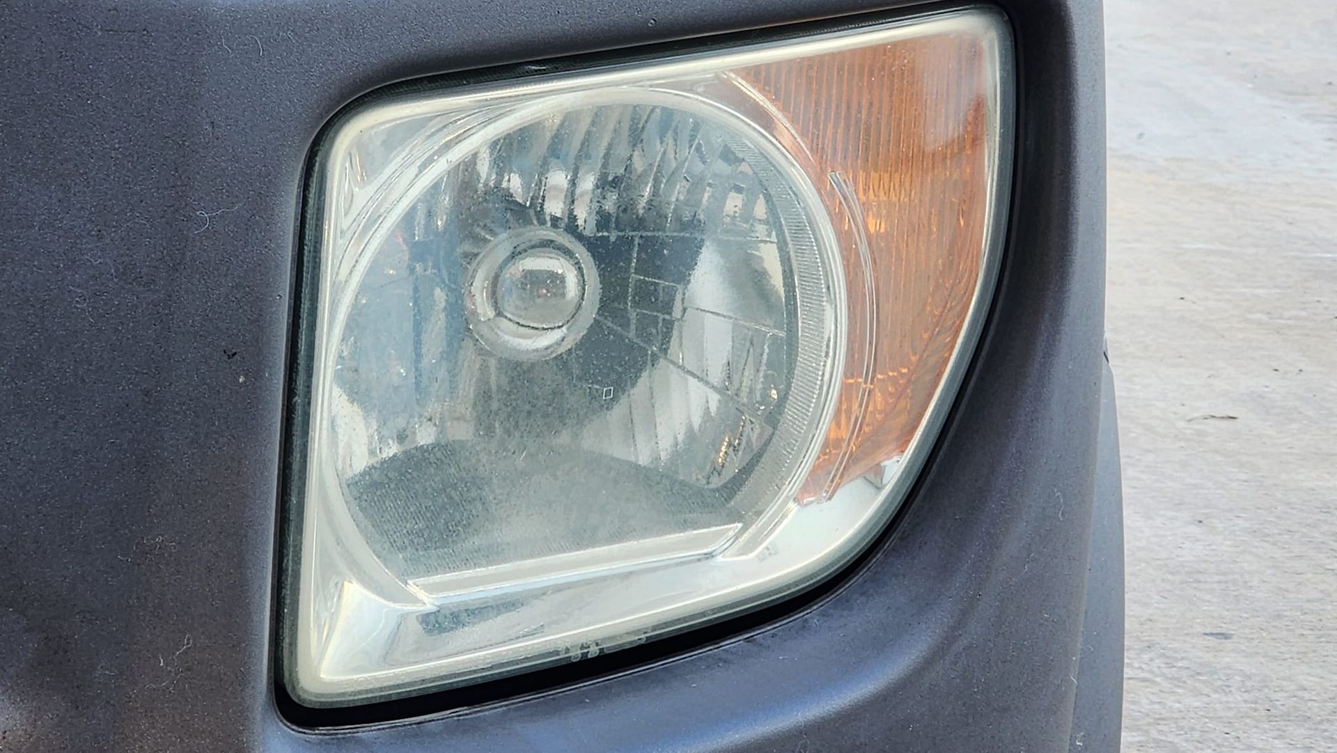 Close-up of a cloudy car headlight with an orange side marker.