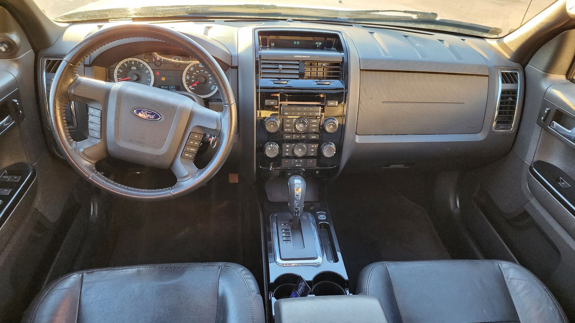 Interior view of a Ford car dashboard; steering wheel, radio controls, gear shift visible.