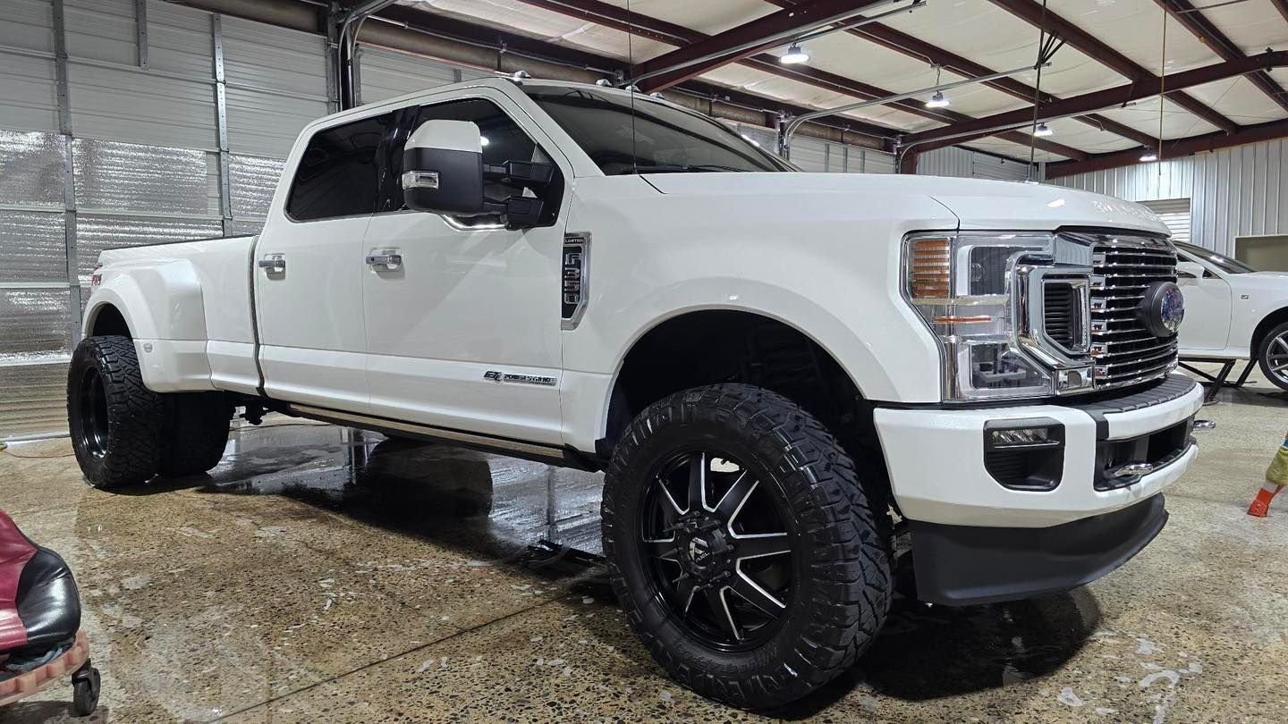 White Ford dually pickup truck with black wheels parked indoors.