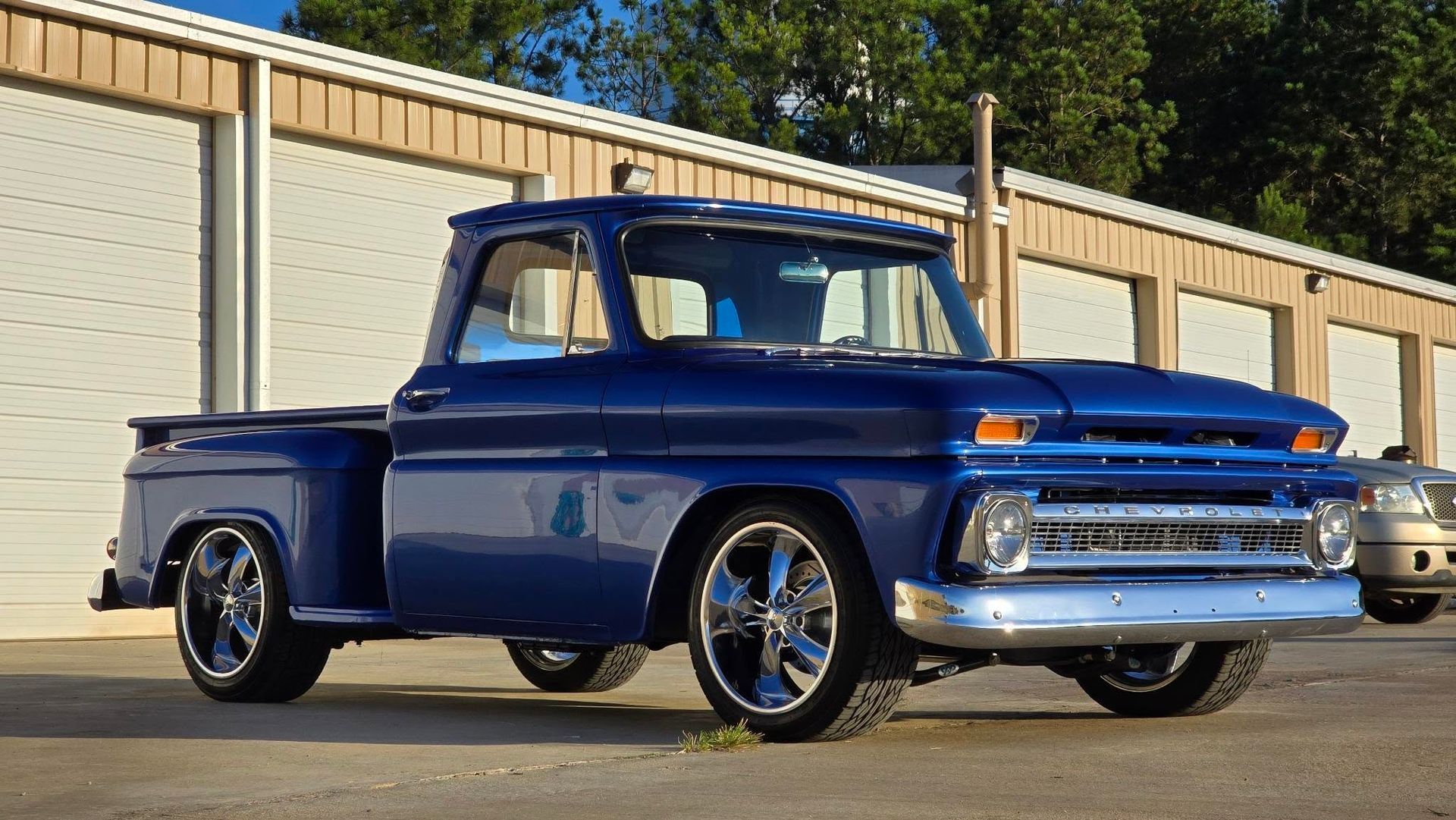 Blue vintage Chevrolet pickup truck with chrome wheels parked near storage units.