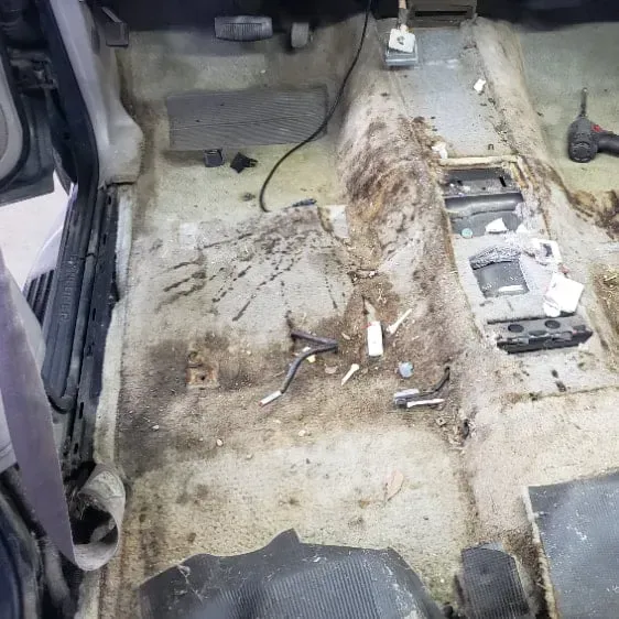 Car interior with dirty carpet and exposed floor components.
