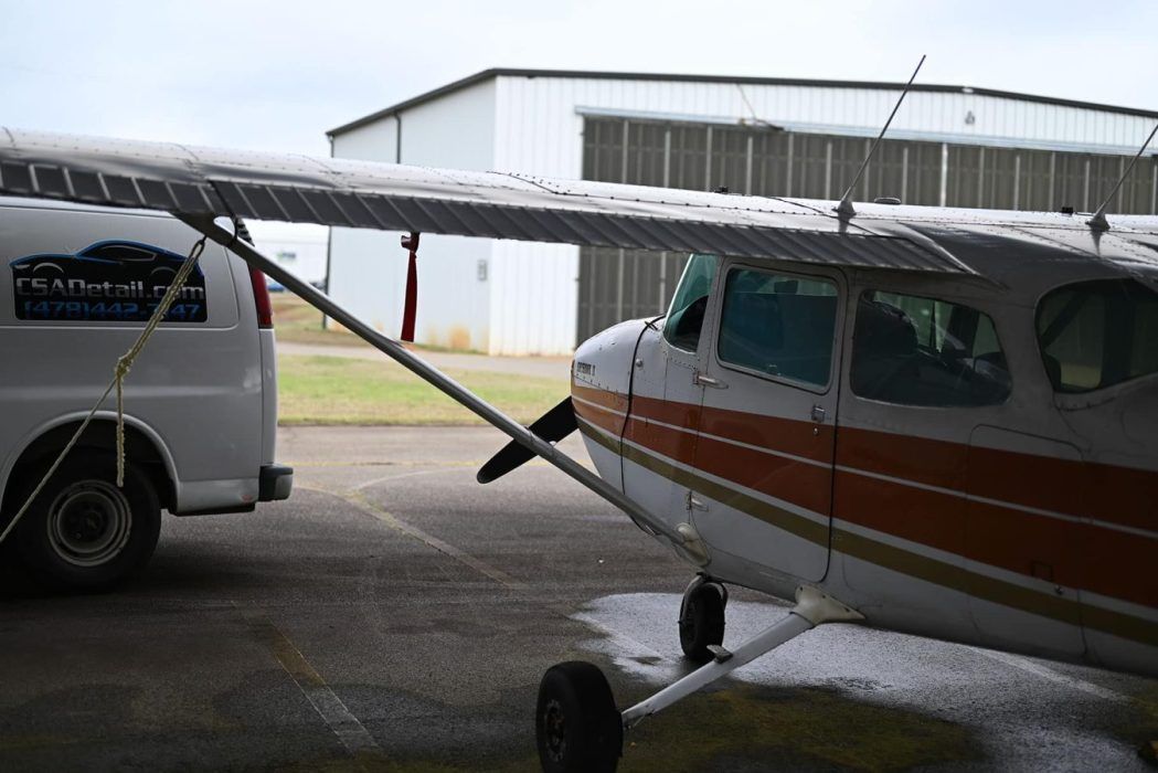 White and orange airplane parked outside a hangar, next to a white van.