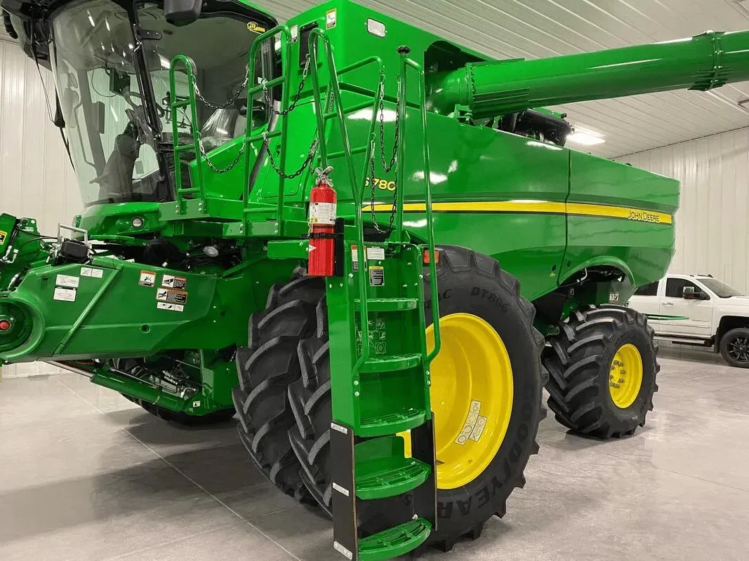 Green John Deere combine with yellow wheels and a ladder, parked inside a building.