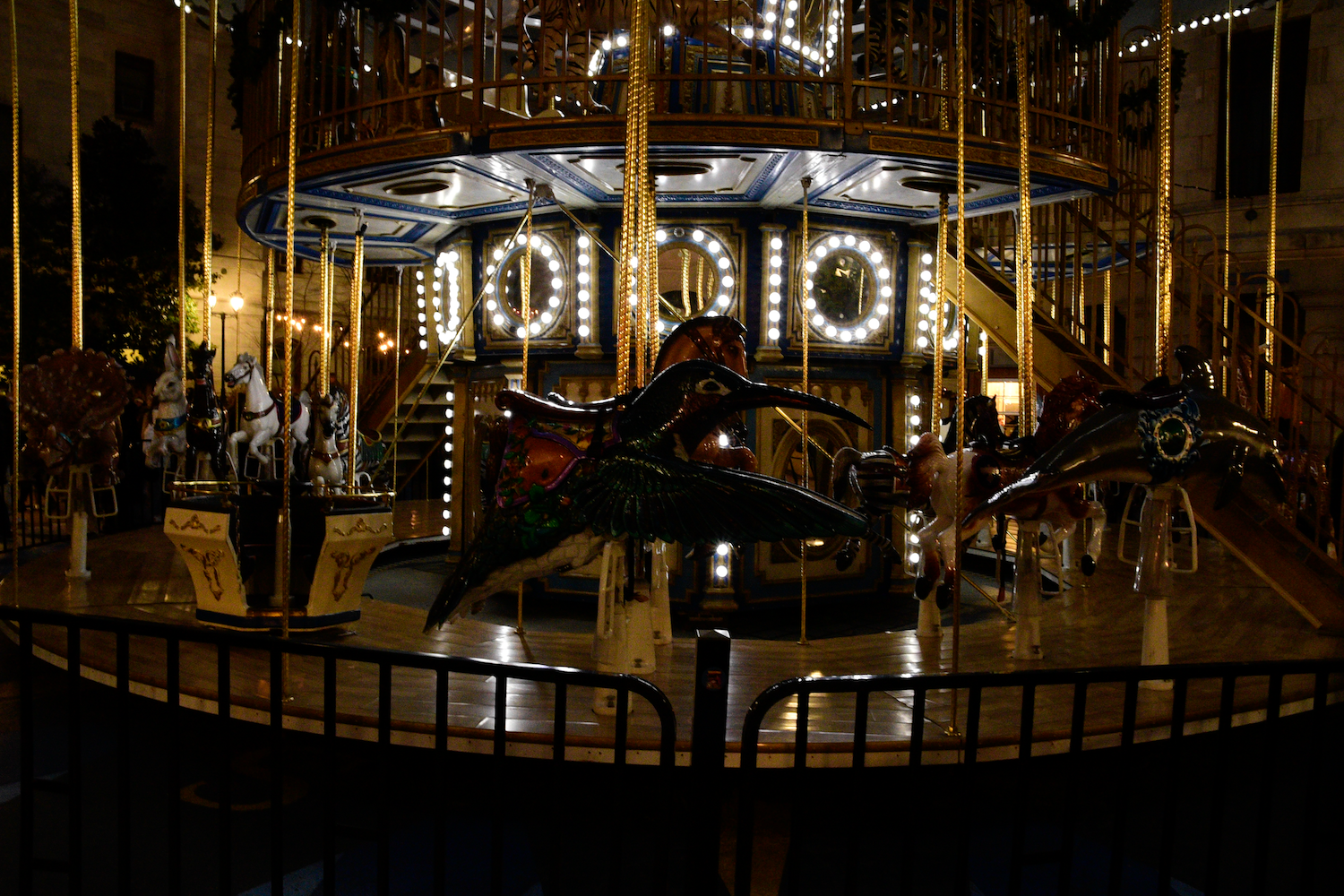A carousel with illuminated lights at night. Figures are silhouetted against the bright lights.