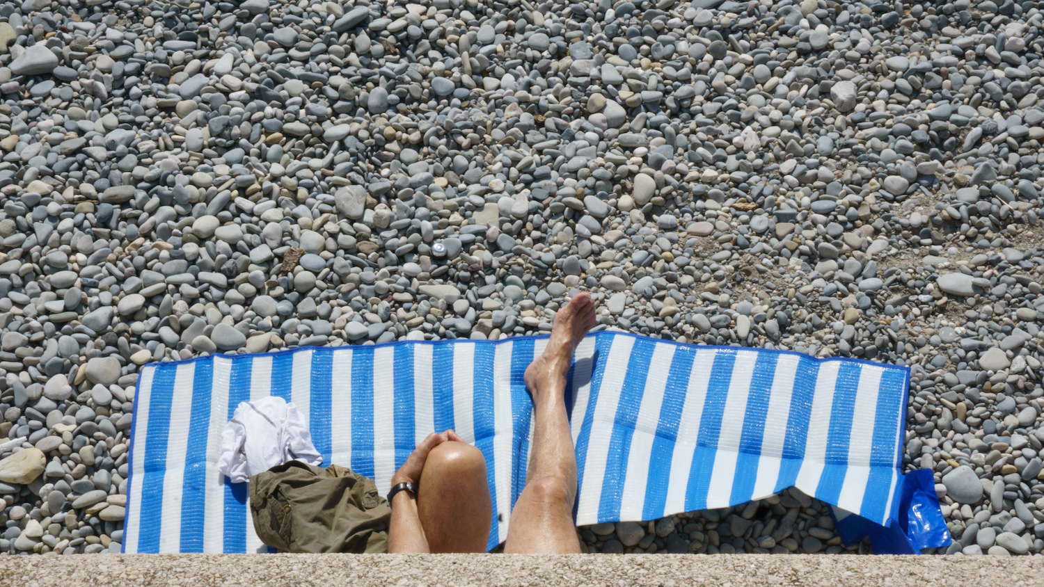 Person sunbathing on a blue and white striped towel at a pebble beach.
