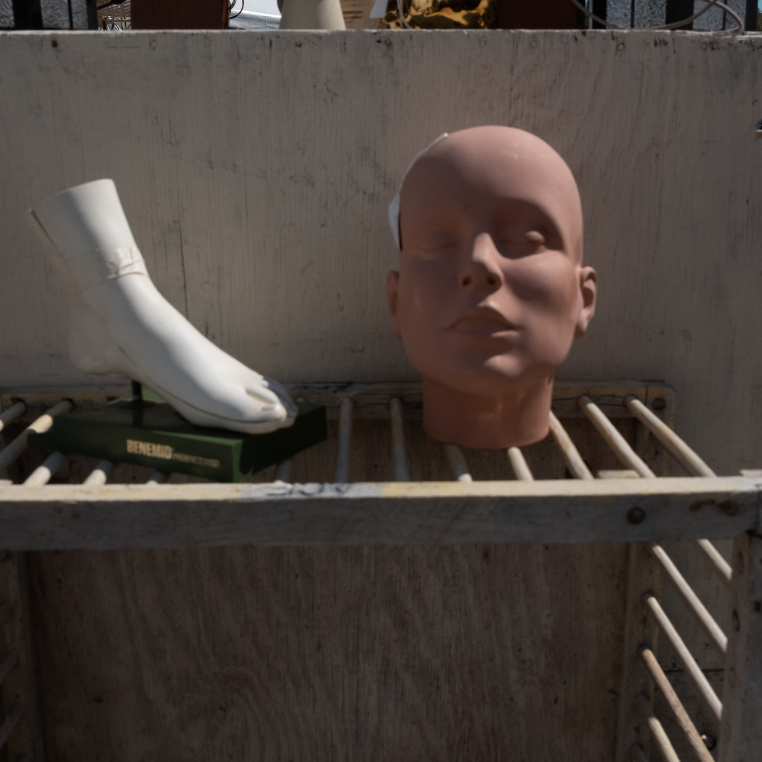Mannequin head and foot on a weathered, wooden shelf; outdoor setting.