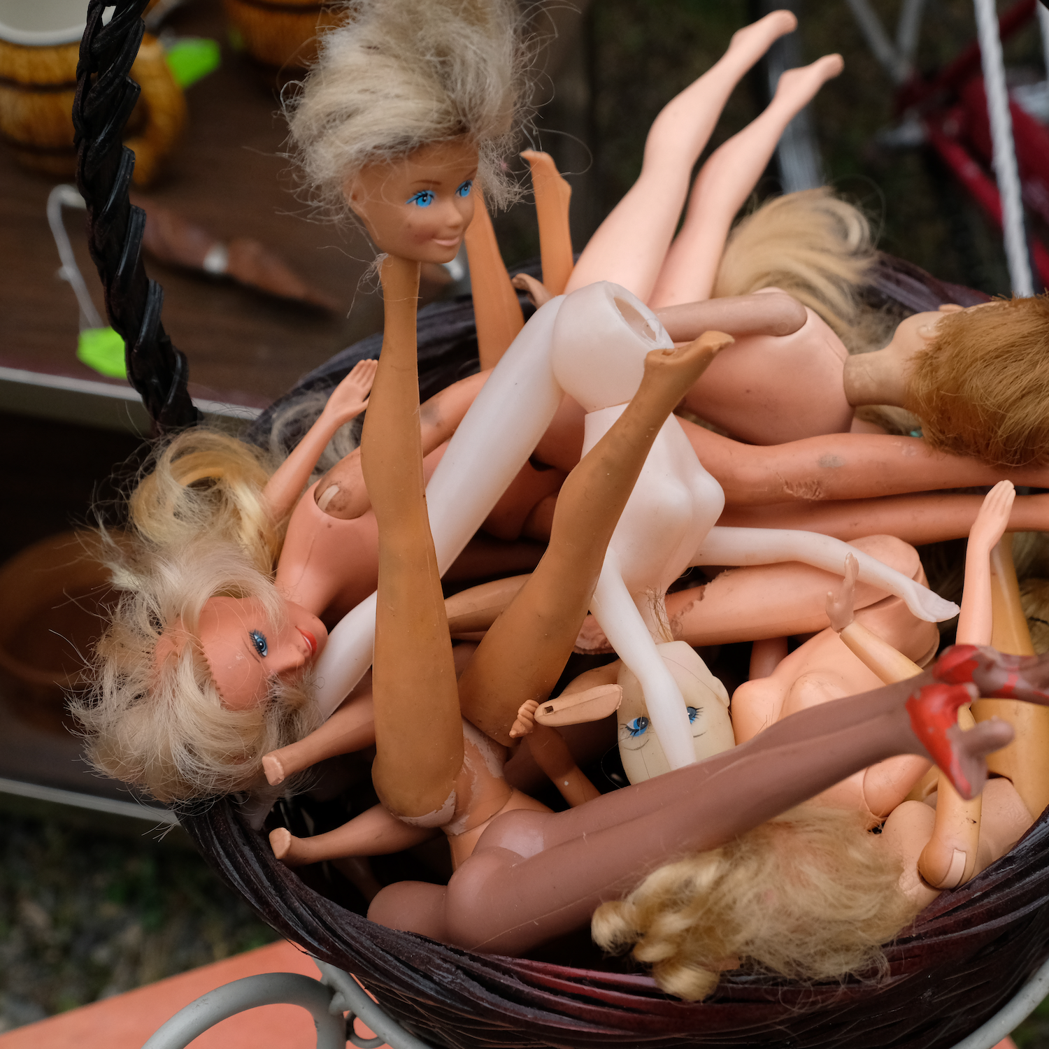 Basket overflowing with disassembled dolls: heads, legs, and torsos in varying skin tones.