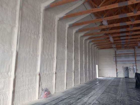 Interior of a building with walls insulated by light-colored foam and wooden beams.