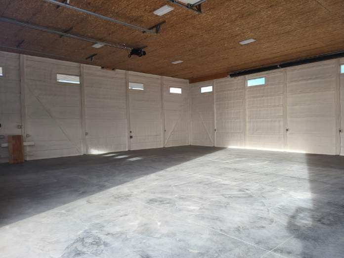 Empty concrete warehouse with a light-colored ceiling and walls, and small rectangular windows along the top of the walls.