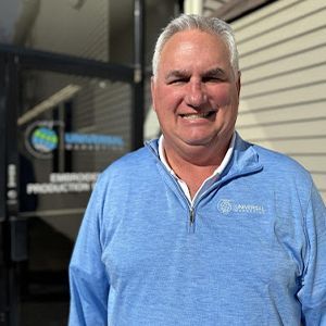A man in a blue sweater is smiling in front of a building.