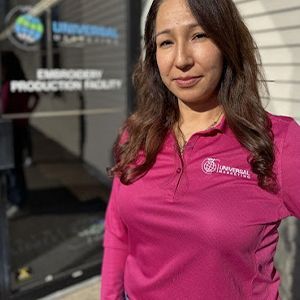 A woman in a pink shirt is standing in front of a building.