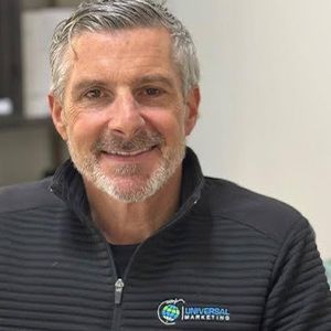 A man with a beard is wearing a black jacket and smiling for the camera.