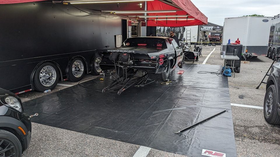 Drag racing car parked outside a black trailer, under a red awning. | Zoom Automotive