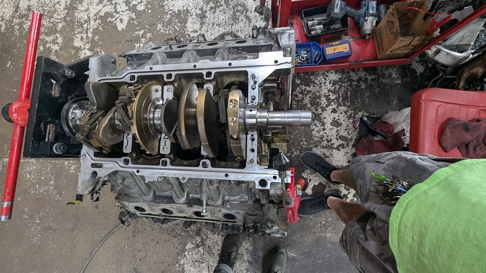 Engine block with crankshaft and connecting rods, in a garage setting. | Zoom Automotive