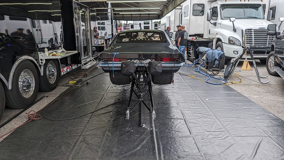 Drag racing car on a dolly, surrounded by trailers and people in a race setting. | Zoom Automotive