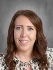 A woman with long brown hair is smiling for the camera while wearing a floral shirt.