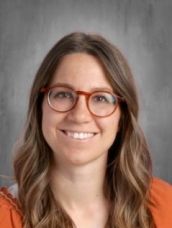 A woman wearing glasses and an orange shirt is smiling for the camera.