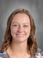 A woman is smiling for a picture and wearing a necklace.