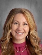 A woman wearing a red shirt and a necklace is smiling for the camera.