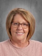 A woman wearing glasses and a pink sweater is smiling for the camera.
