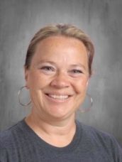 A woman wearing hoop earrings and a gray shirt is smiling for a picture.