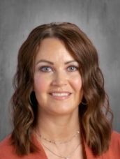 A woman with long brown hair and a necklace is smiling for the camera.