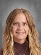 A woman with long blonde hair and a necklace is smiling for the camera.