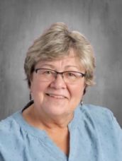 A woman wearing glasses and a blue shirt is smiling for the camera.