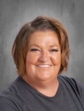 A woman in a gray shirt is smiling for the camera.