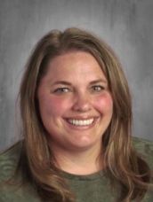 A woman in a green shirt is smiling for the camera.