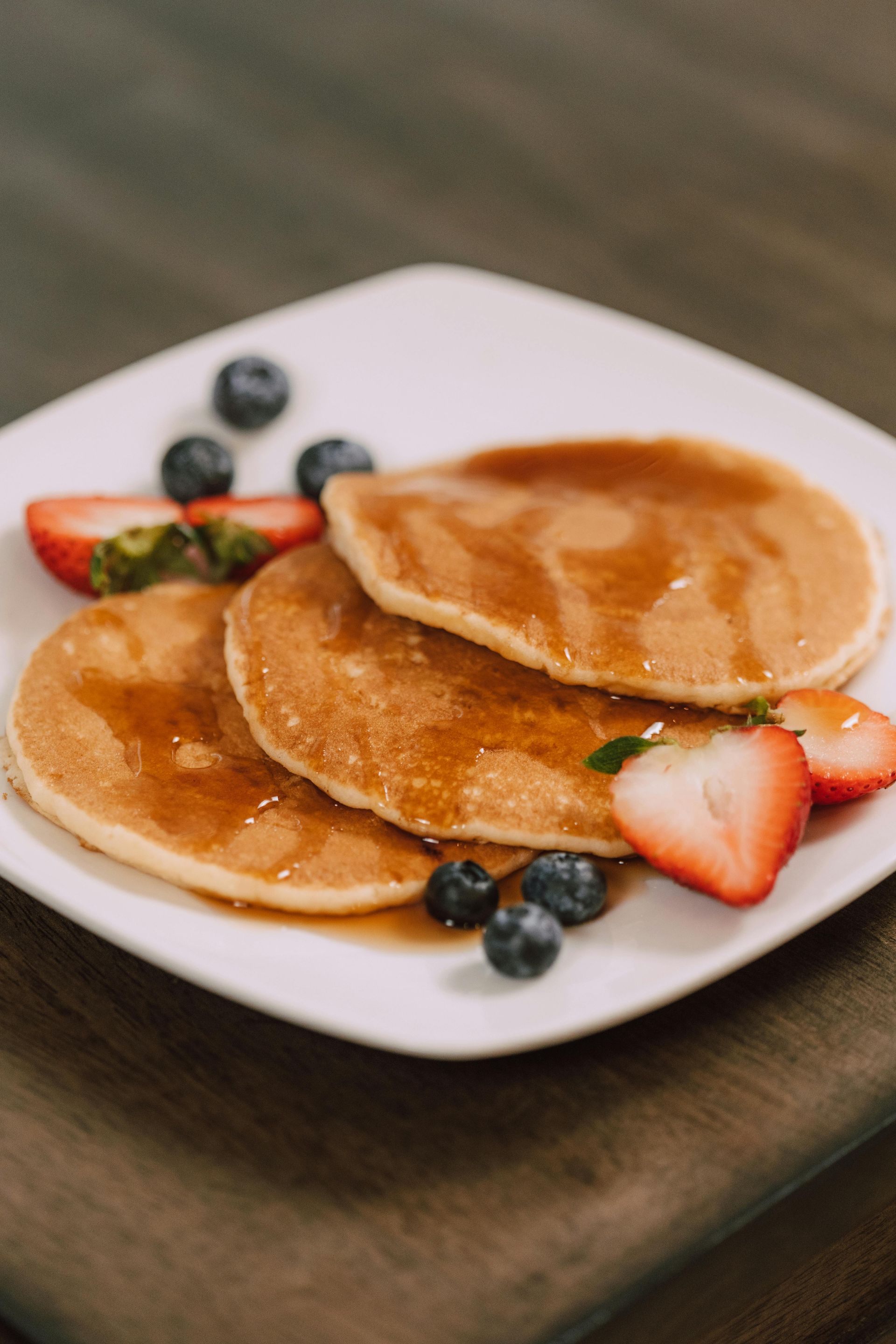 A white plate topped with pancakes , syrup , strawberries and blueberries.