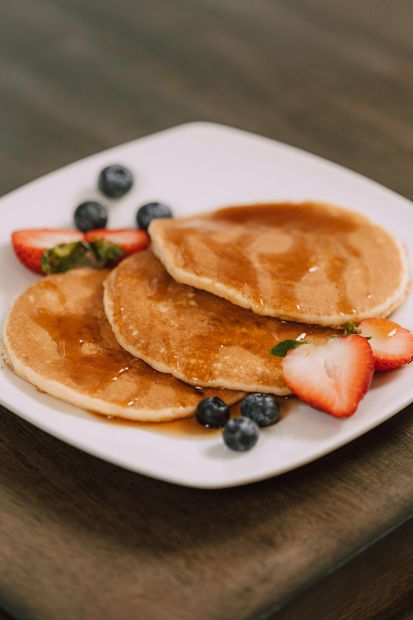 A white plate topped with pancakes , syrup , strawberries and blueberries.
